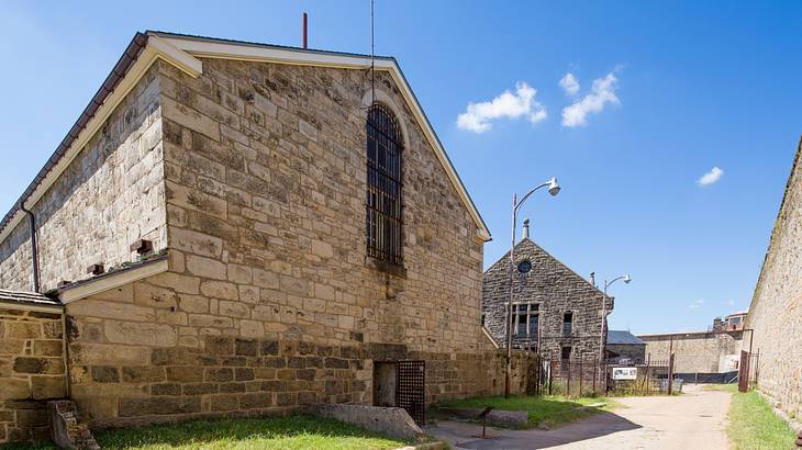 Stone buildings next to a path and grass under a blue sky with some clouds