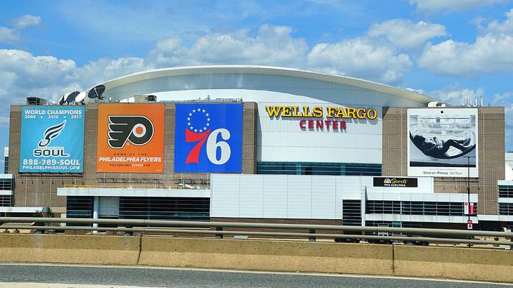 A stadium with sports banners on it next to a road under a blue sky with clouds