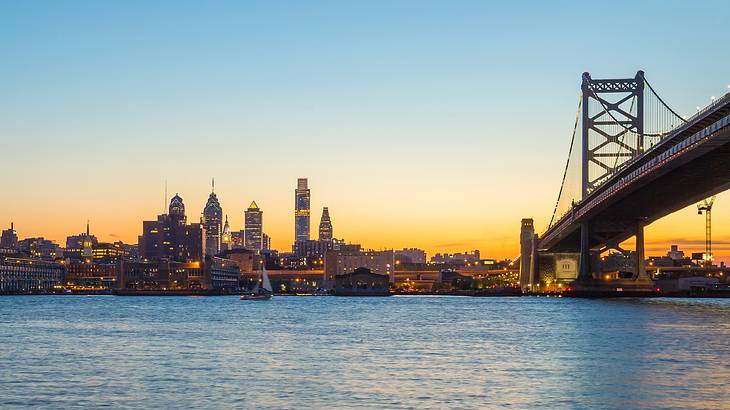 An illuminated city next to a bridge and a river at sunset