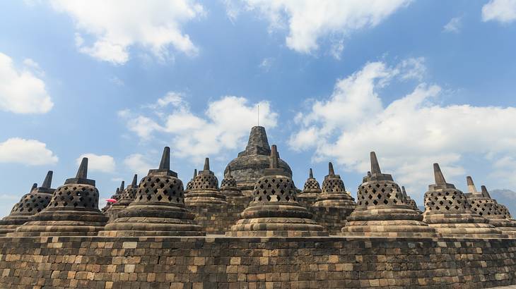 Top view of many pointy tops of a stone temple against a partly cloudy sky