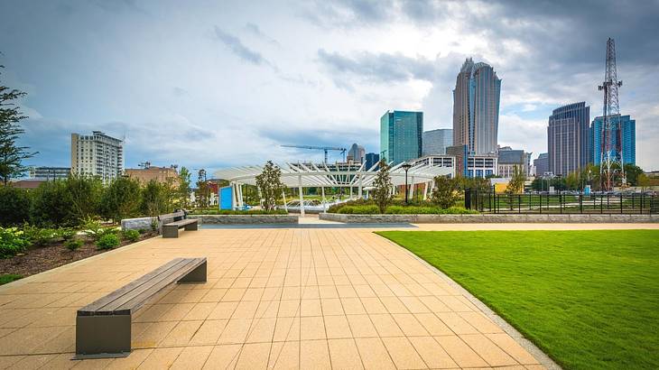 A path with a bench on it and grass with a city skyline in the background