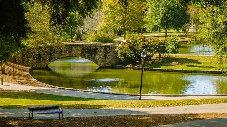 A park with a path, a lake with a bridge over it, and lots of green trees