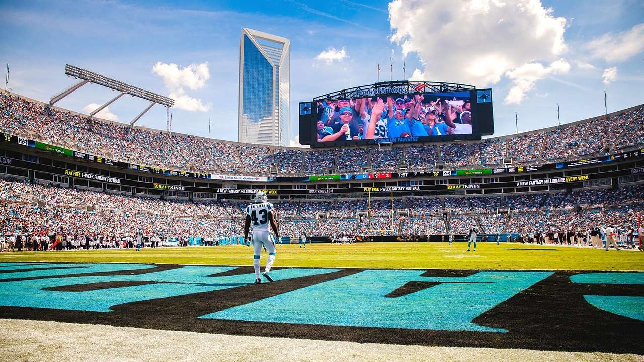 A football stadium with black and turquoise writing on the field and a game in play