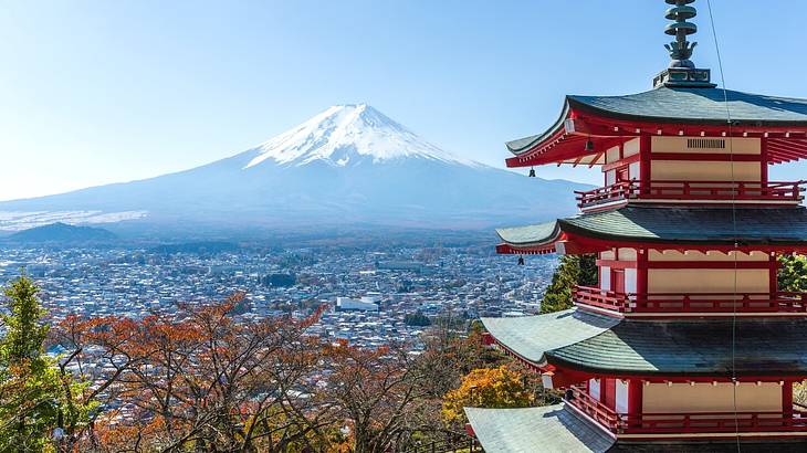 A tall snow-capped mountain at the back with a city, trees and a pagoda in front A tall snow-capped mountain at the back with a city, trees and a pagoda in front