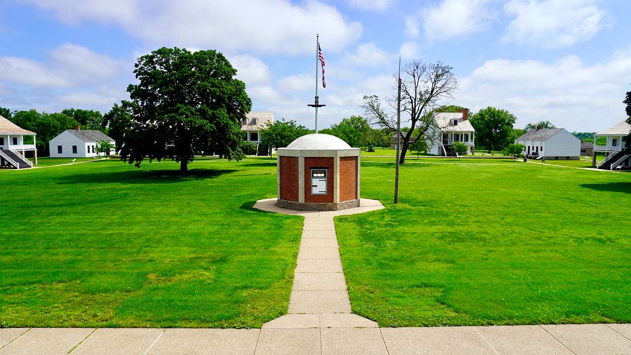 A short structure with the American flag on top in the middle of a lush park