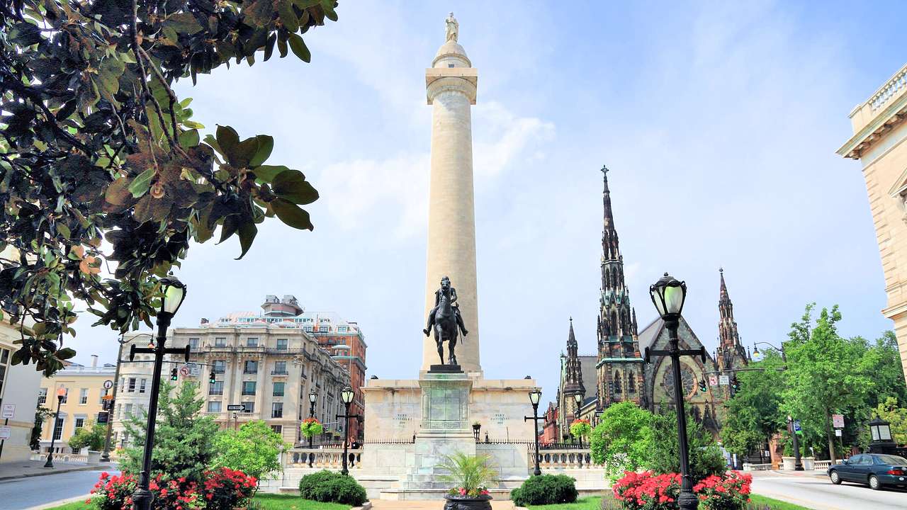 A small park with a bronze statue of an equestrian and a tall monument near buildings