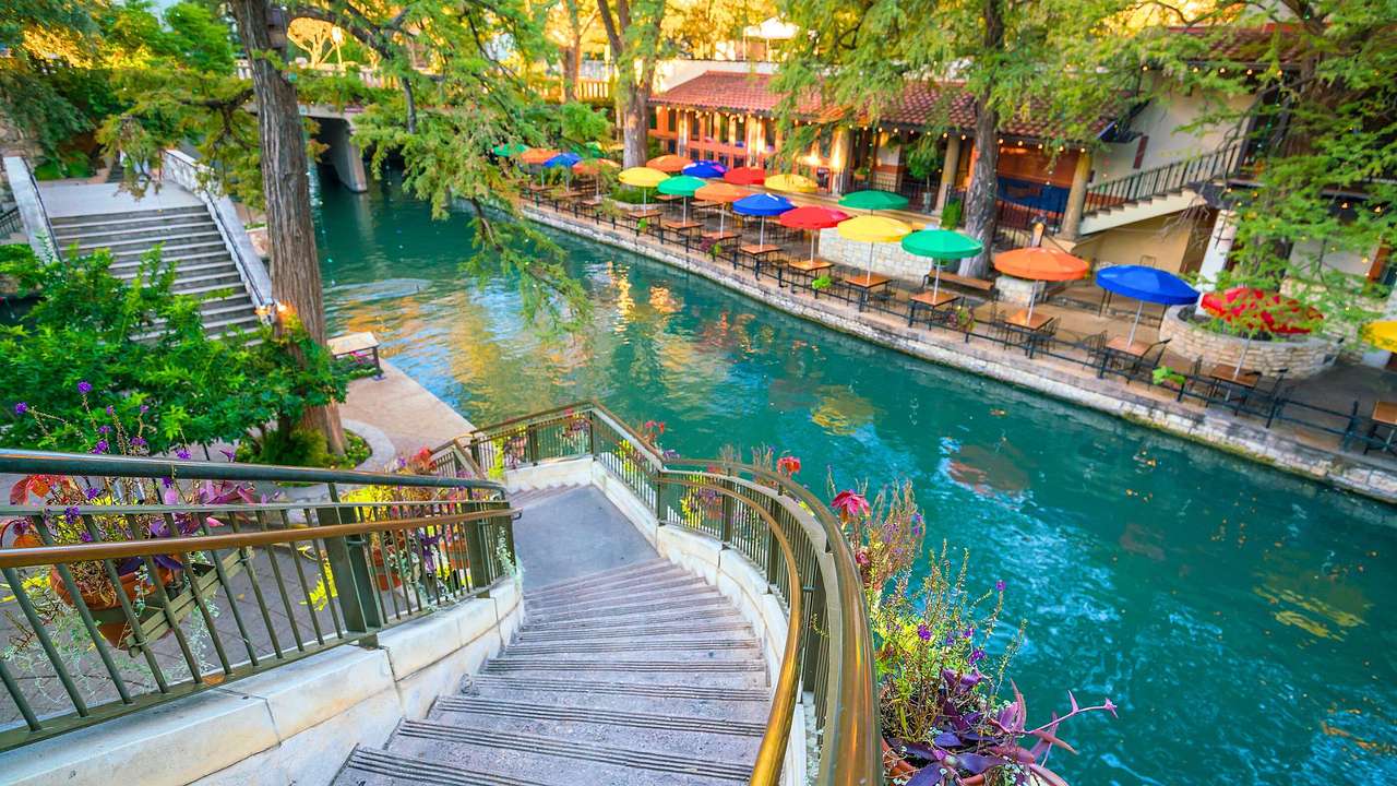 A concrete staircase leading to a riverwalk near a river and colorful parasols