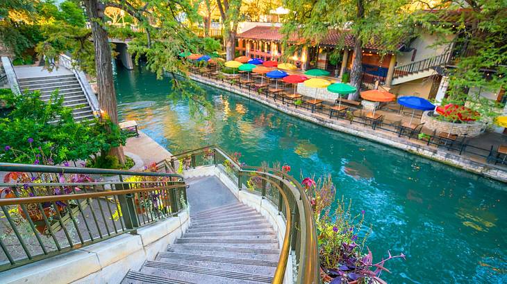 A concrete staircase leading to a riverwalk near a river and colorful parasols