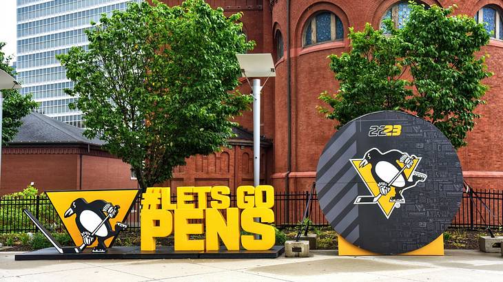 A large hockey puck sculpture with a penguin image and a "#Lets Go Pens" sign