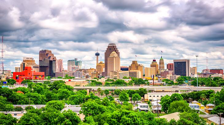 A city skyline with green trees in front of it on a cloudy day