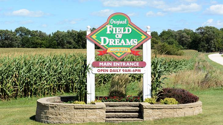 A sign saying "Original Field of Dreams Main Entrance" with a field and trees behind