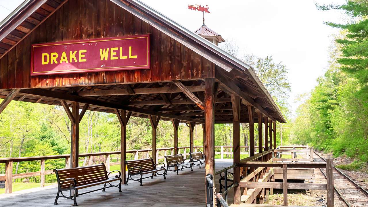 An old wooden pavilion structure with benches and a sign saying "Drake Well"