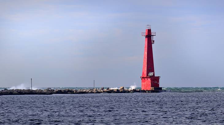 A red lighthouse near a rocky pathway and the ocean