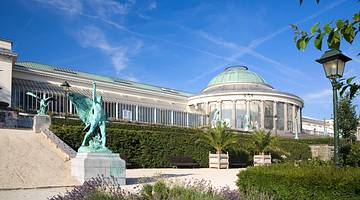 The outside of a greenhouse with green hedges and statues in front