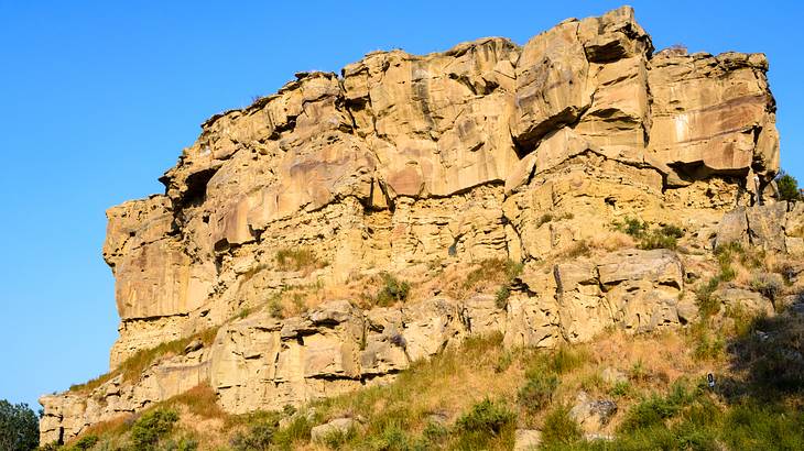 A massive sandstone formation with greenery at its foot on a clear day