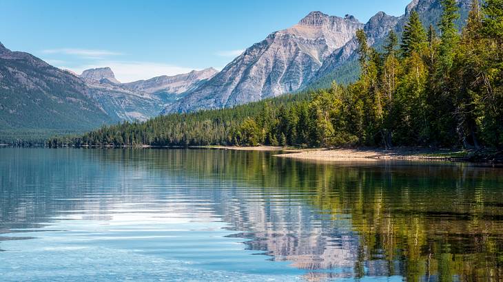 Mountains and lakeside trees reflected over the glassy water showing the rocks below