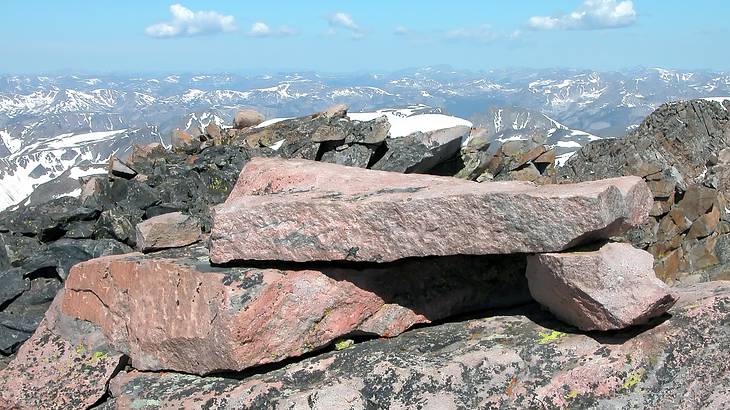 Piles of rocks on a mountain peak overlooking snowy mountains