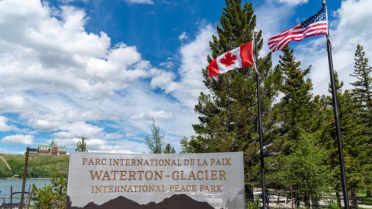 Flags of Canada and USA at the right side of a park signage with trees in the back