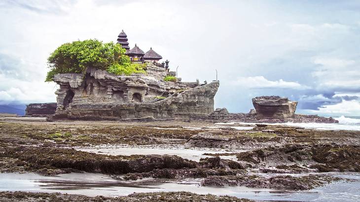 A temple on a rock with trees surrounded by more rocks and waves