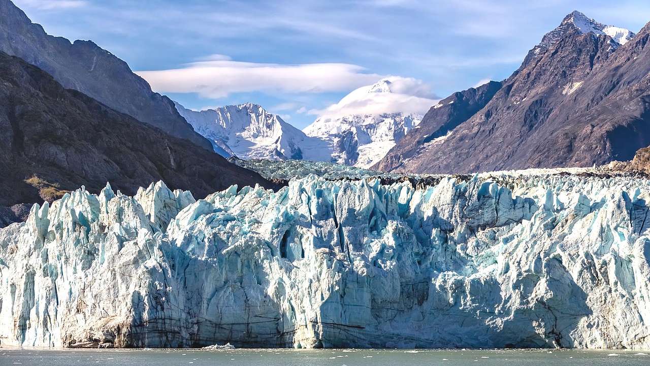 Blue ice formations against tall, gray, snow-capped mountains