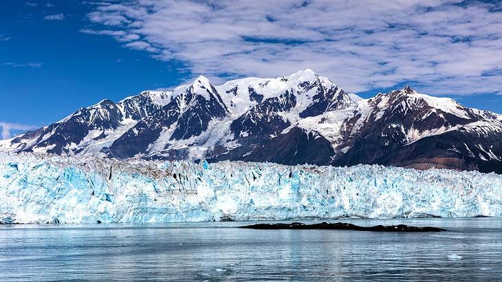 Ice formations against a tall snow-capped mountain overlooking water