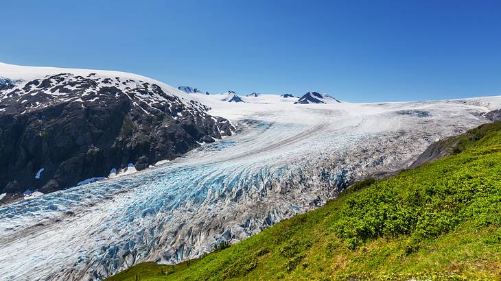 Looking at an inclined glacier between mountains covered with greenery