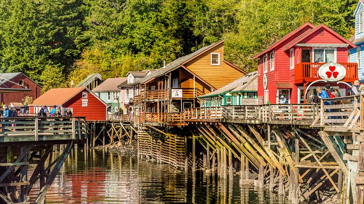 Multi-color hut-shaped wooden houses over water, against green trees