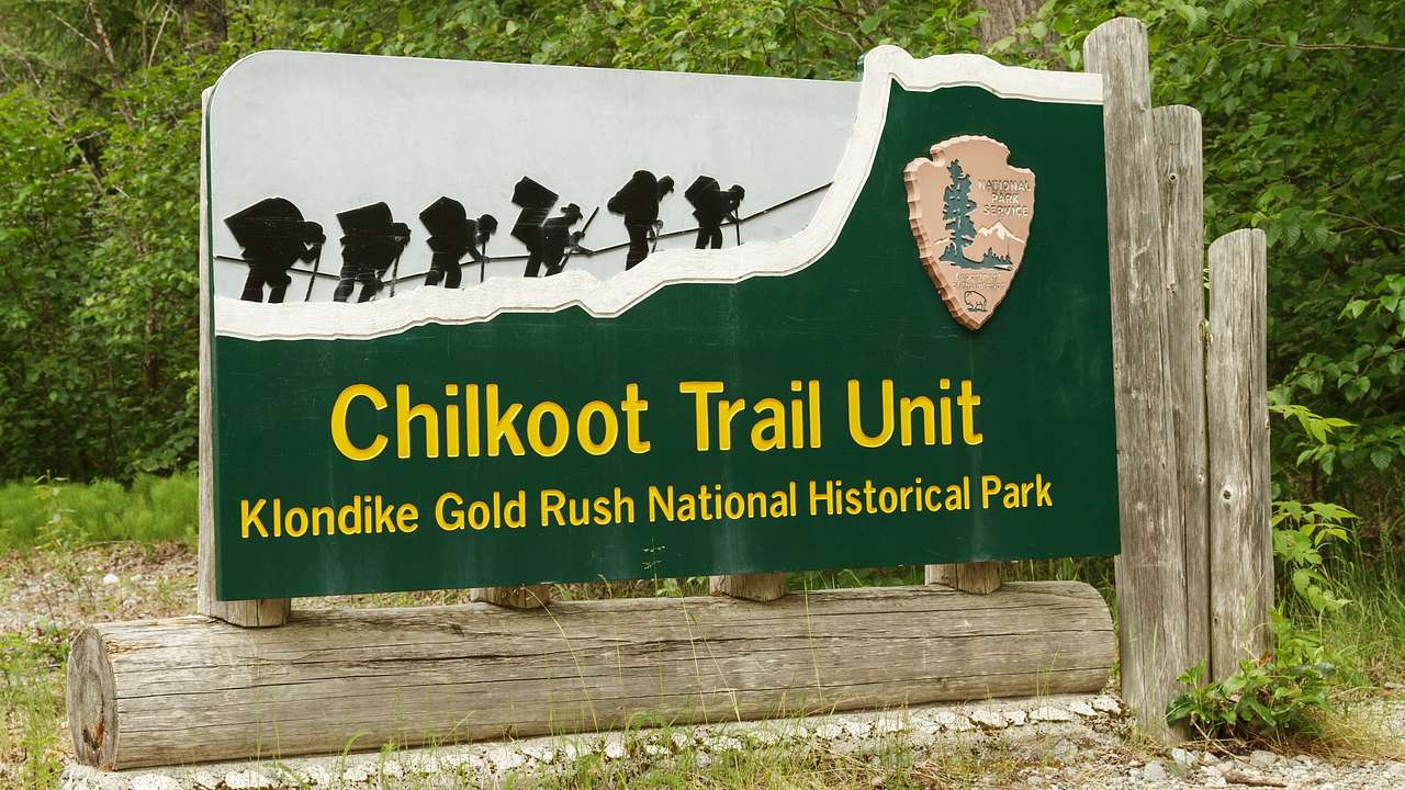 A green sign saying "Chilkoot Trail Unit" against green trees