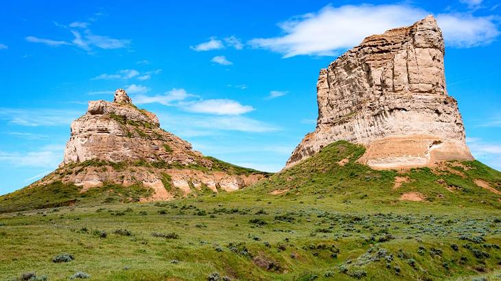 Two rock features with green grass around them under a blue sky with clouds