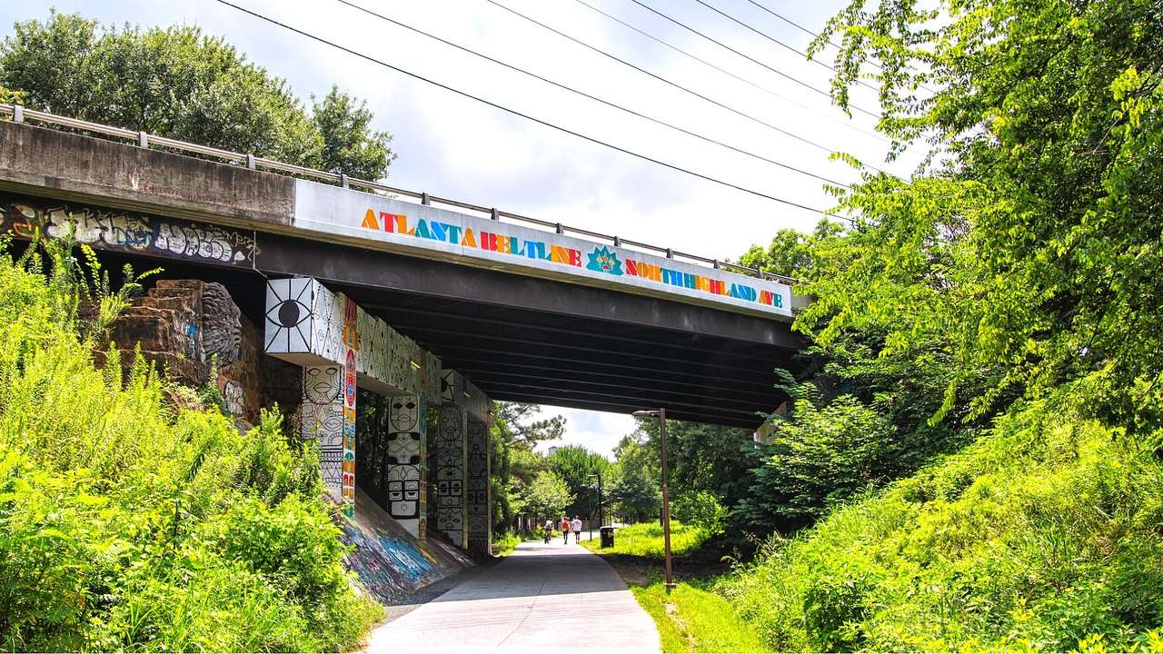 A bridge with colorful street art on it over a tree-lined path