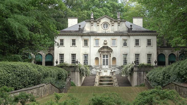 A white manor house with steps in front of it and greenery surrounding it