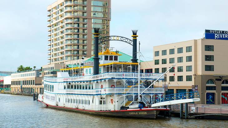 A white paddle wheeler docked at a port against buildings, under the blue sky