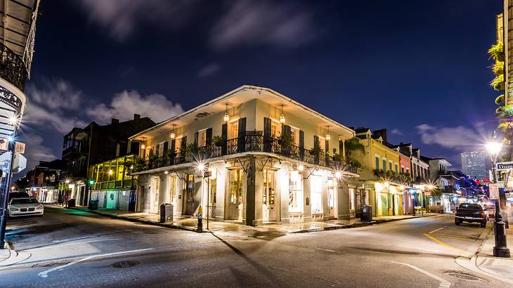 A two-story white building with bright lights on the corner of a street at night