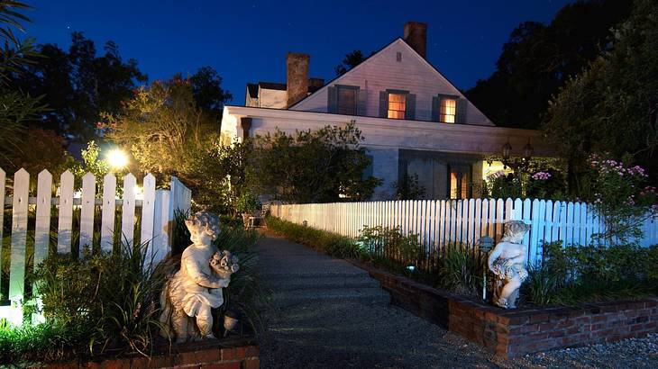 A walkway to a white vernacular house, bordered with a white fence