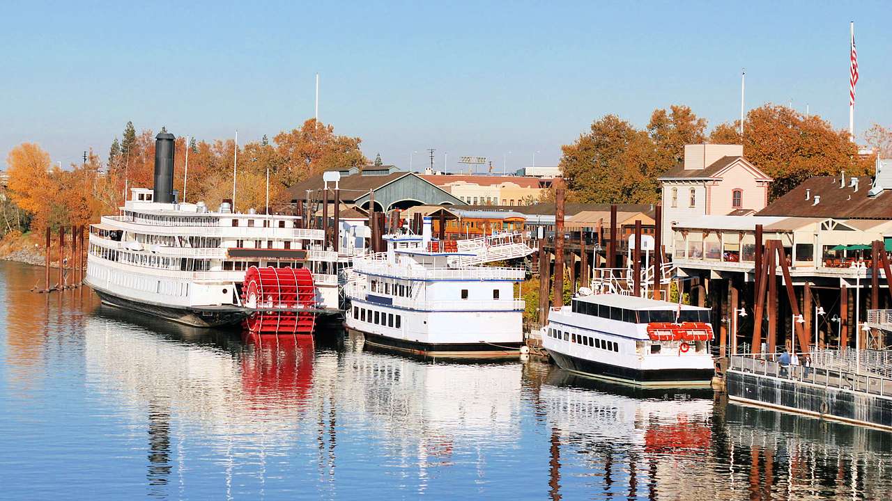 White riverboats moored near coastal establishments and autumn trees