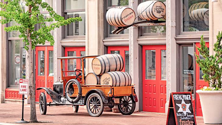 Bourbon barrels on an old cart parked in front of a building with red doors