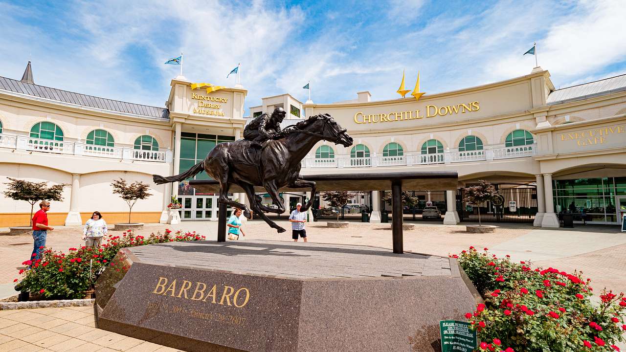 A statue of an equestrian near roses and a building with a "Churchill Downs" sign