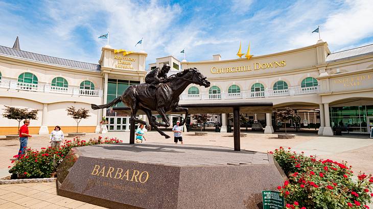 A statue of an equestrian near roses and a building with a "Churchill Downs" sign