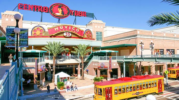 A facade of a building next to palm trees and a red and yellow tram