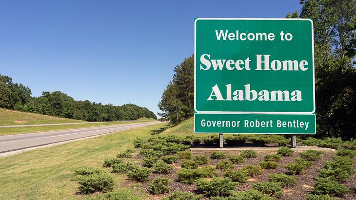 A green and white sign with greenery around that says, "Sweet Home Alabama"