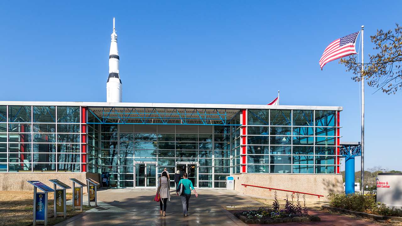A glass building with a US flag to its right and a rocket ship at the back