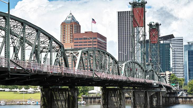 A truss bridge over a body of water with a city skyline in the background