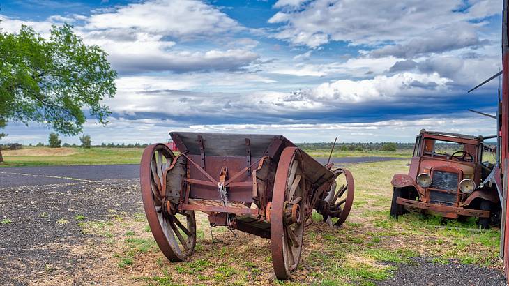 A rusty wagon and truck in an abandoned area under a blue sky with clouds