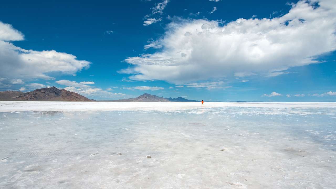 Vast salt flats with a person standing on them in the distance next to mountains