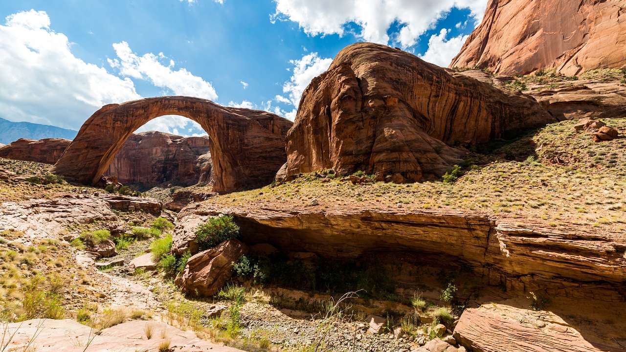 A red sandstone arch surrounded by red rock mountains framed by a blue sky