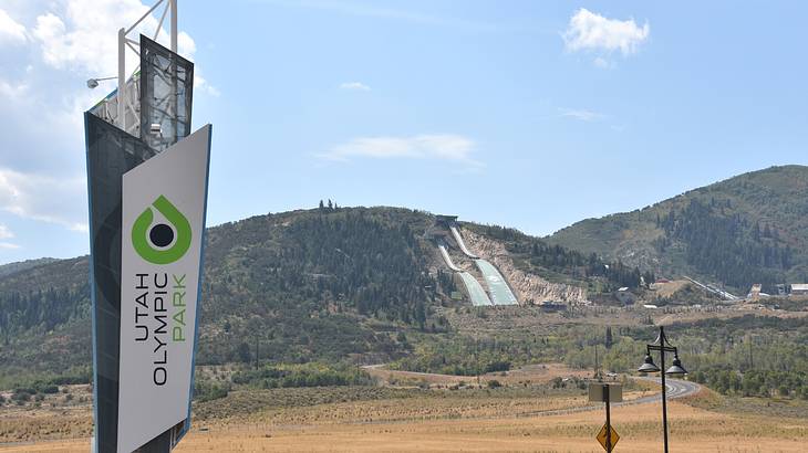 A sign that says "Utah Olympic Park" next to a hill under a blue sky