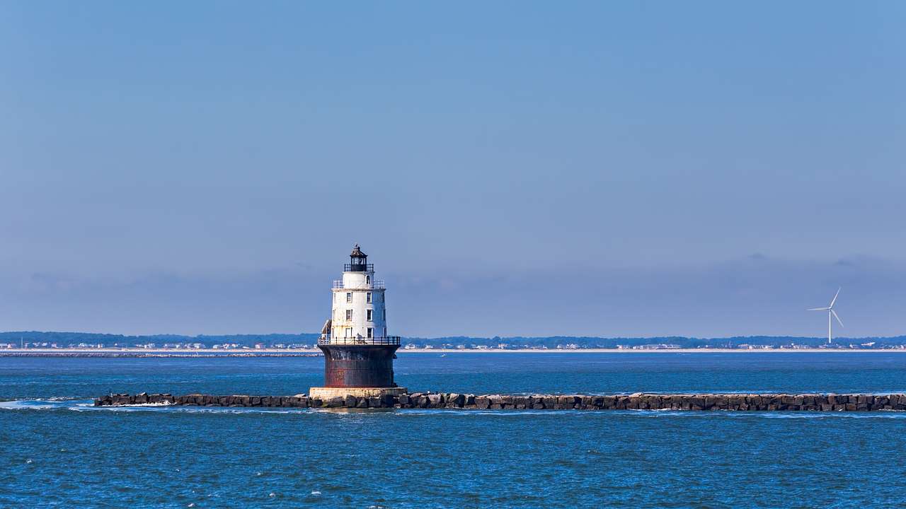 A small lighthouse in a bay of water with a wind turbine in the distance