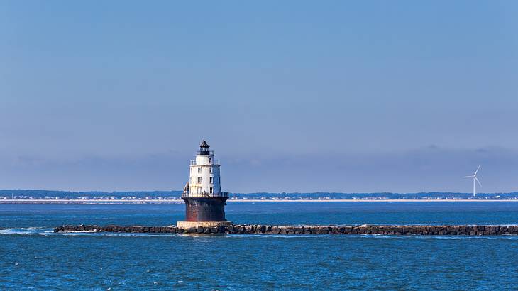 A small lighthouse in a bay of water with a wind turbine in the distance