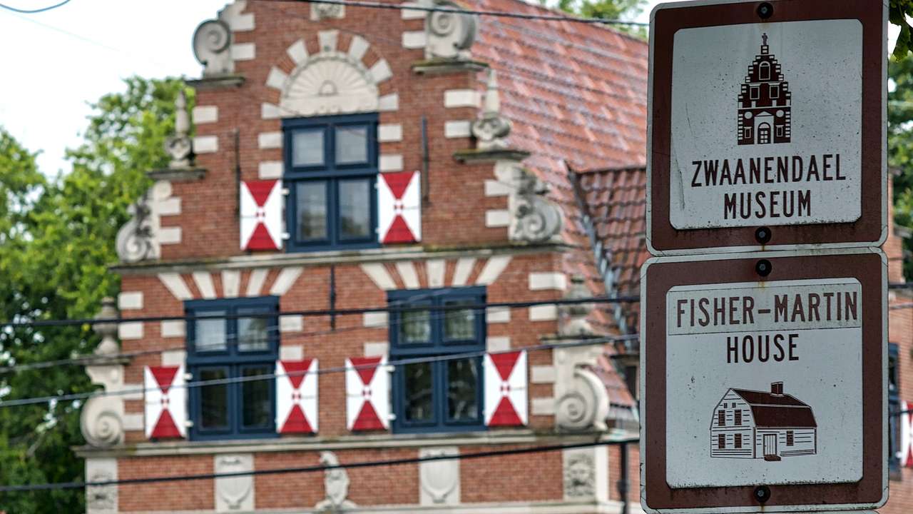 A red brick house with red and white details next to white and brown signs