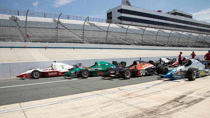 A race track with multiple racecars on the track next to empty stands